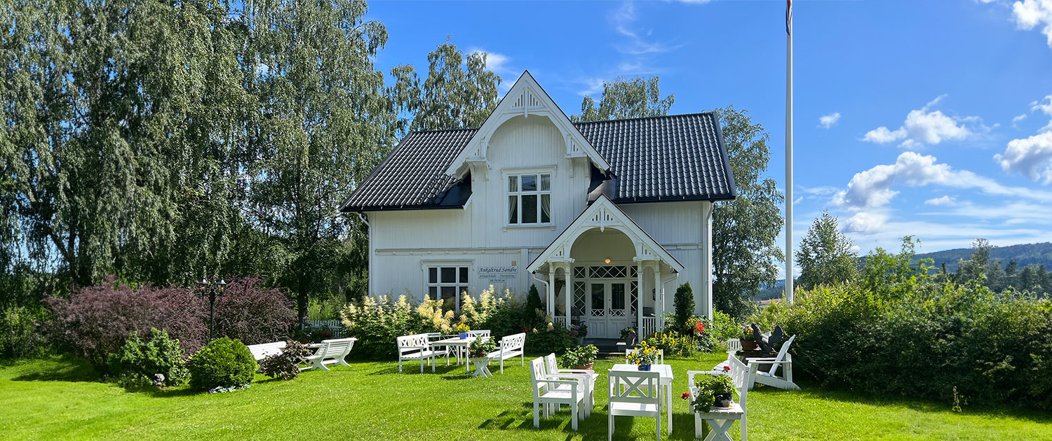 Ankaltrud Søndre med flott hage og sittegrupper foran Kårboligen en sommerdag med sol og blå himmel.
